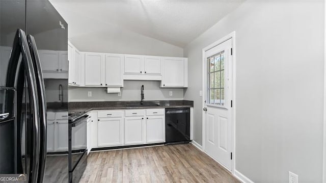 kitchen with dark countertops, black appliances, lofted ceiling, white cabinetry, and a sink