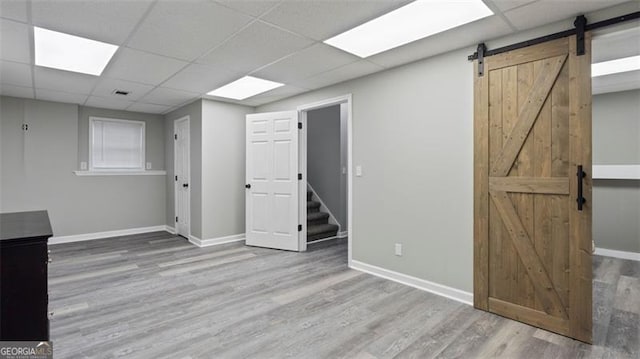 below grade area featuring a paneled ceiling, a barn door, and wood finished floors