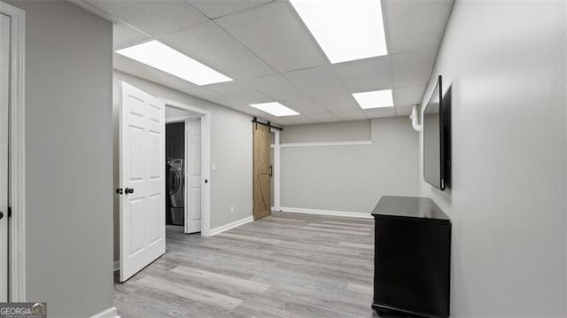 interior space featuring a barn door, washer / clothes dryer, a drop ceiling, and light wood finished floors