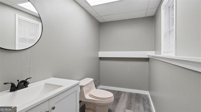 bathroom with baseboards, a drop ceiling, toilet, wood finished floors, and vanity