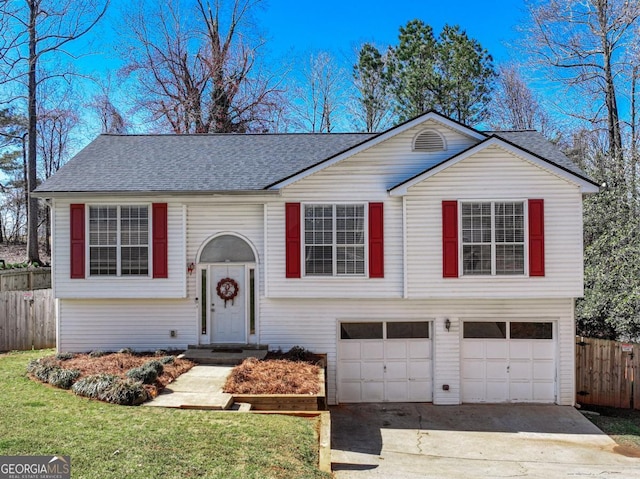 split foyer home featuring an attached garage, a shingled roof, a front lawn, fence, and driveway