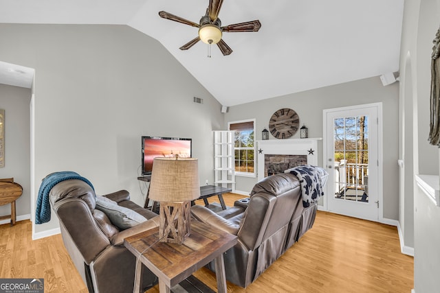 living room with visible vents, high vaulted ceiling, light wood-style flooring, a stone fireplace, and ceiling fan