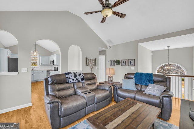 living room featuring light wood-type flooring, arched walkways, high vaulted ceiling, and ceiling fan with notable chandelier