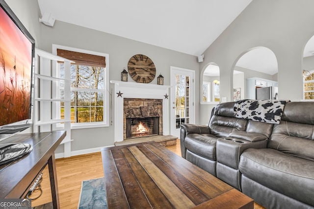 living room with a stone fireplace, light wood-style flooring, high vaulted ceiling, and baseboards