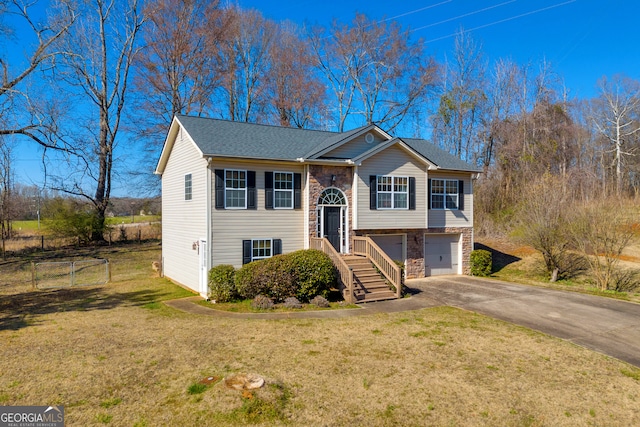 bi-level home featuring aphalt driveway, stone siding, fence, an attached garage, and a front yard