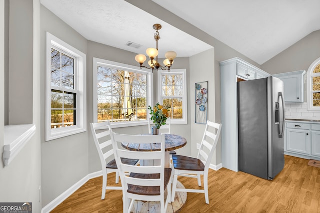 dining area with visible vents, baseboards, light wood-type flooring, lofted ceiling, and a notable chandelier