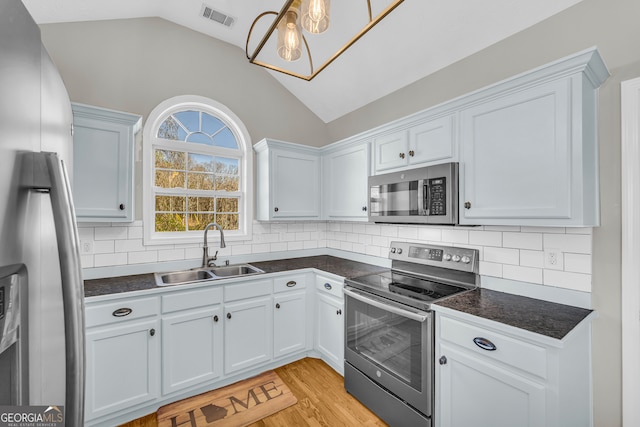 kitchen with visible vents, a sink, dark countertops, stainless steel appliances, and vaulted ceiling