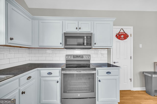 kitchen with baseboards, decorative backsplash, light wood-style floors, appliances with stainless steel finishes, and dark countertops