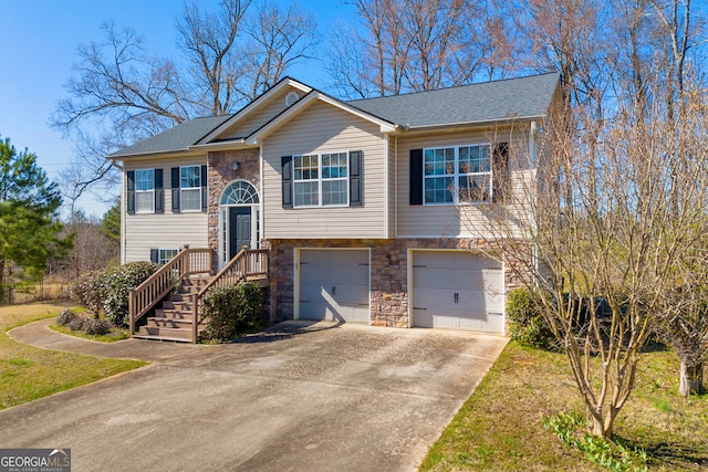 split foyer home featuring a garage, stone siding, driveway, and roof with shingles