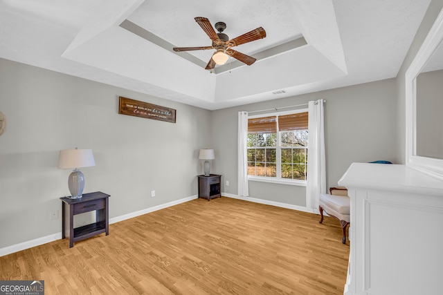 sitting room featuring a tray ceiling, light wood-style floors, and baseboards