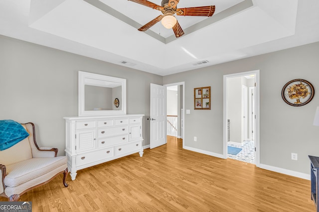 living area featuring a tray ceiling, baseboards, visible vents, and light wood finished floors