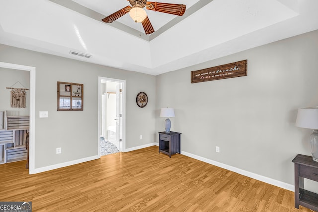 living room with visible vents, ceiling fan, baseboards, light wood-type flooring, and a raised ceiling