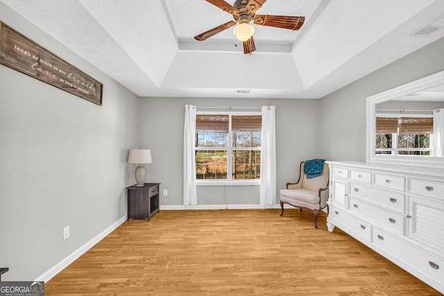 unfurnished room with visible vents, baseboards, light wood-type flooring, a raised ceiling, and a ceiling fan