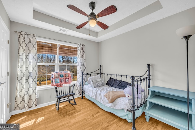 bedroom with visible vents, a raised ceiling, baseboards, and wood finished floors