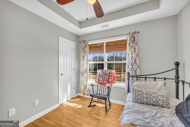 bedroom featuring visible vents, baseboards, light wood-style floors, and a tray ceiling