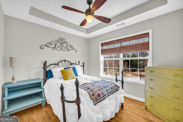 bedroom with visible vents, a textured ceiling, a raised ceiling, and light wood-style floors