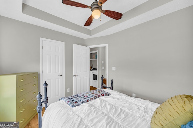 bedroom with ceiling fan, a tray ceiling, and wood finished floors