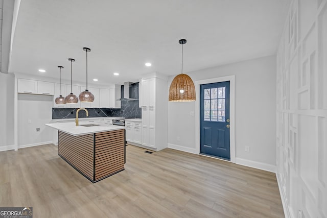 kitchen featuring a sink, wall chimney range hood, light wood finished floors, decorative backsplash, and light countertops