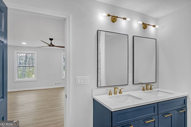 full bath with double vanity, wood finished floors, ceiling fan, and a sink