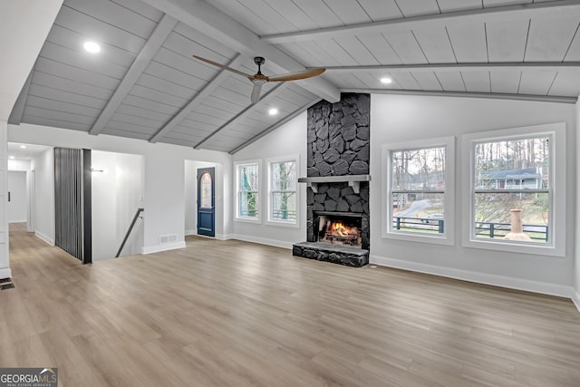 unfurnished living room featuring wood finished floors, a stone fireplace, baseboards, ceiling fan, and vaulted ceiling with beams