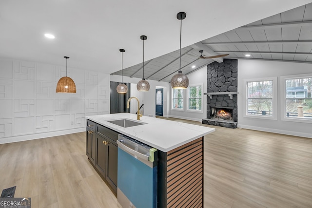 kitchen featuring lofted ceiling with beams, a sink, a stone fireplace, dishwasher, and light wood-type flooring