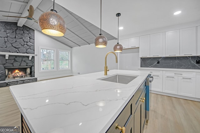 kitchen featuring a sink, light wood-style flooring, vaulted ceiling with beams, and white cabinets