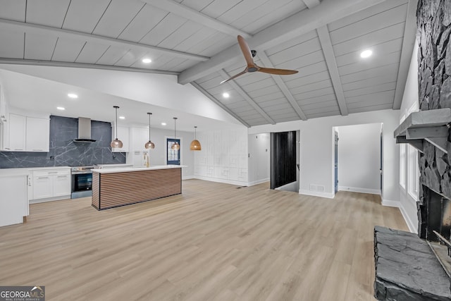 kitchen featuring wall chimney range hood, ceiling fan, open floor plan, stainless steel electric stove, and a stone fireplace