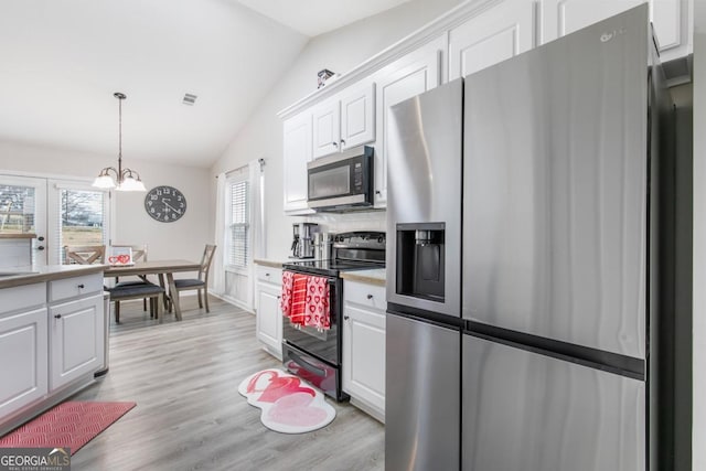 kitchen with light wood finished floors, lofted ceiling, appliances with stainless steel finishes, pendant lighting, and white cabinetry