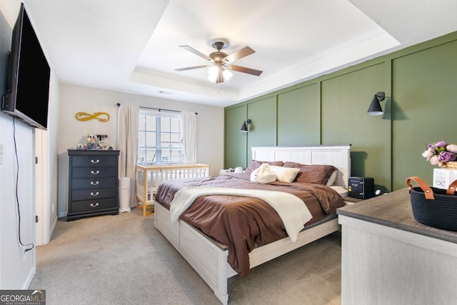 bedroom featuring light carpet, a ceiling fan, a tray ceiling, crown molding, and a decorative wall