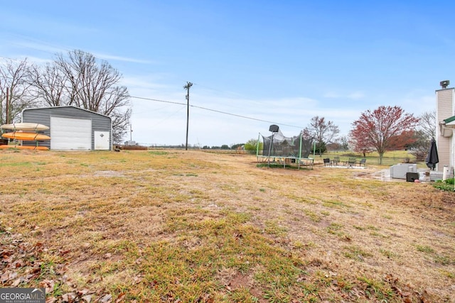 view of yard with a garage, a trampoline, and an outdoor structure