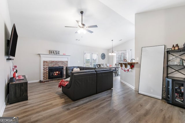 living room featuring a brick fireplace, baseboards, ceiling fan with notable chandelier, wood finished floors, and high vaulted ceiling