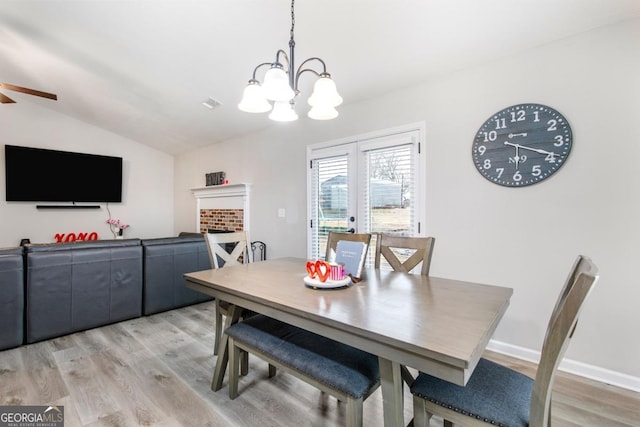 dining room featuring light wood-type flooring, a notable chandelier, a fireplace, baseboards, and vaulted ceiling