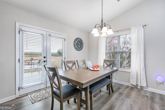 dining space featuring lofted ceiling, wood finished floors, baseboards, and a chandelier