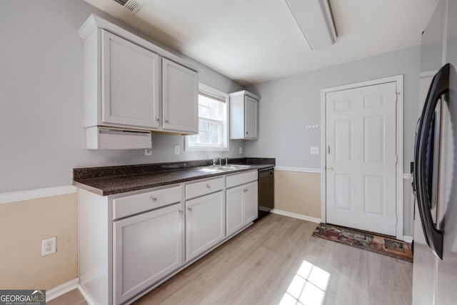 kitchen featuring light wood-style flooring, a sink, dark countertops, black dishwasher, and freestanding refrigerator