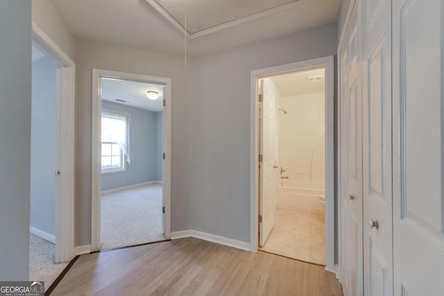 hall featuring light wood-style flooring, attic access, and baseboards