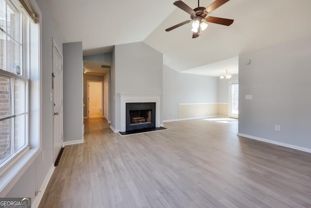 unfurnished living room featuring wood finished floors, baseboards, lofted ceiling, a fireplace, and ceiling fan with notable chandelier