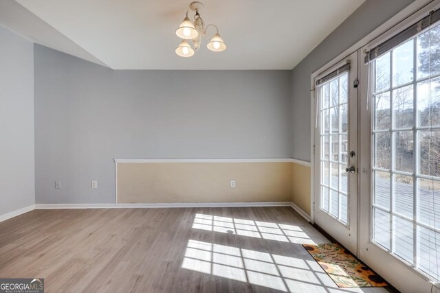 unfurnished dining area featuring french doors, baseboards, wood finished floors, and a chandelier