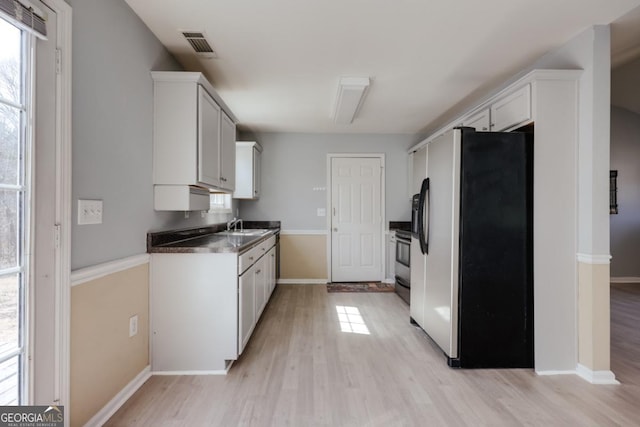 kitchen with light wood finished floors, visible vents, baseboards, stainless steel fridge, and a sink