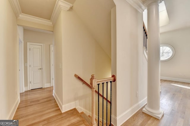 stairway with decorative columns, wood finished floors, baseboards, and ornamental molding