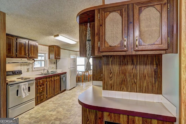 kitchen with under cabinet range hood, light countertops, white appliances, a textured ceiling, and a sink