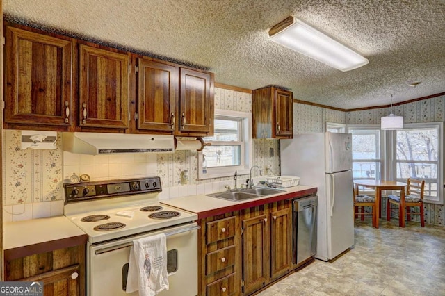 kitchen featuring under cabinet range hood, a sink, a textured ceiling, white appliances, and wallpapered walls