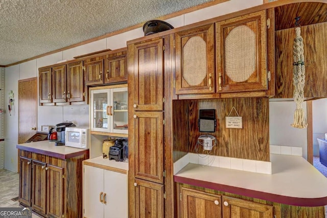 kitchen with light countertops, brown cabinetry, white microwave, and a textured ceiling