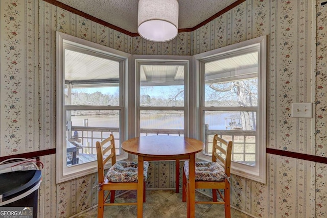 dining area with a water view, a textured ceiling, crown molding, and wallpapered walls