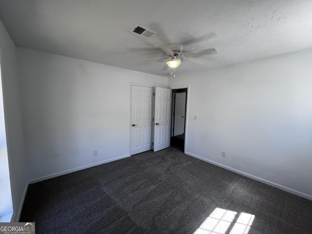 empty room with visible vents, a textured ceiling, dark colored carpet, baseboards, and ceiling fan