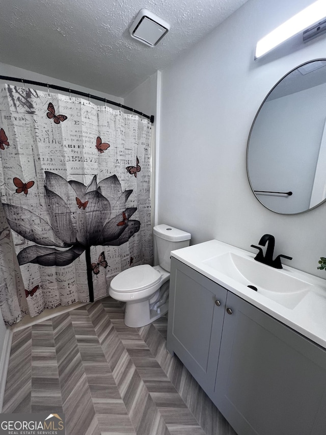 bathroom with a shower with curtain, a textured ceiling, vanity, and toilet