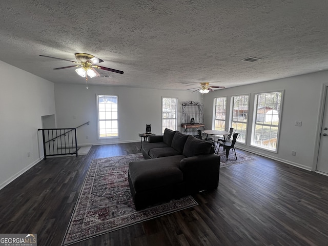 living area featuring visible vents, a textured ceiling, dark wood-style floors, baseboards, and ceiling fan