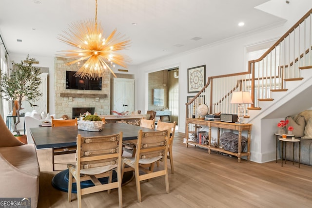 dining area with stairway, light wood-style floors, an inviting chandelier, a fireplace, and crown molding