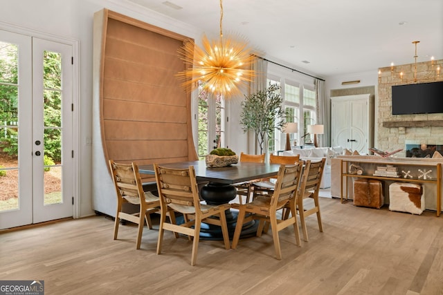 dining space featuring french doors, light wood-style floors, an inviting chandelier, and a fireplace