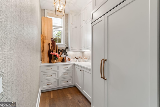 bar featuring a notable chandelier, dark wood finished floors, decorative backsplash, paneled built in refrigerator, and a textured wall