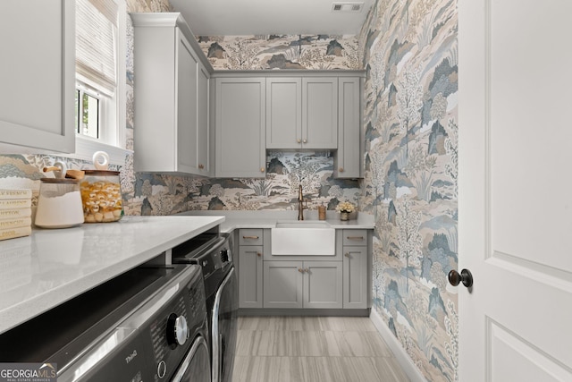 kitchen with a sink, washer and clothes dryer, gray cabinets, and wallpapered walls